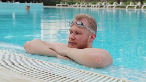 Jovem com repouso de barba na piscina com óculos de natação junto ao hotel — Vídeo de Stock