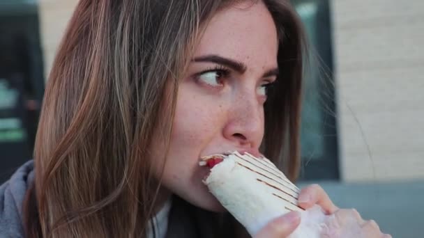 Vrouw bijten shawarma op straat na training in het park, close-up, zijaanzicht — Stockvideo