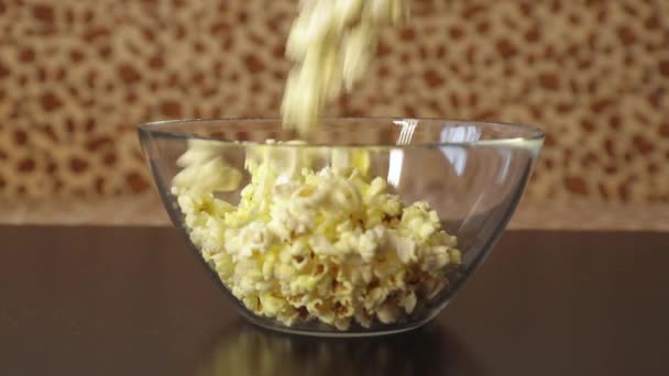 Popcorn faller ner i en glasskål som står på ett träbord — Stockvideo