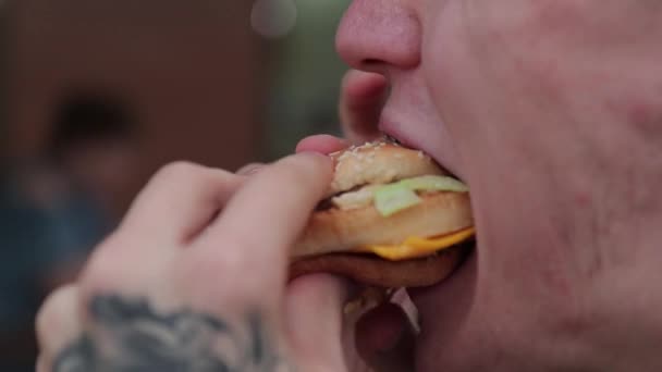 De mond van de man bijt de hamburger af en kauwt er smakelijk op. Sluiten. — Stockvideo