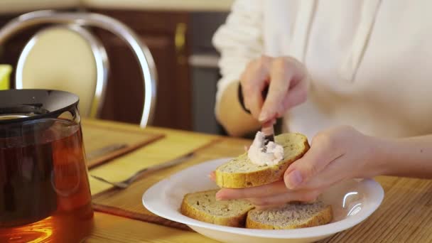 Las manos de la mujer extienden queso cuajada con un cuchillo en el pan en el desayuno — Vídeos de Stock