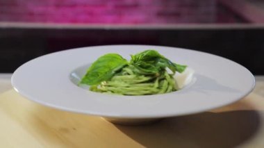 Çam fıstıklı İtalyan makarna, pesto sosu ve beyaz tabakta taze fesleğen.
