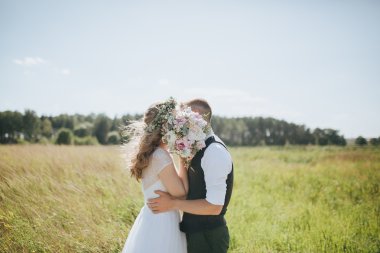adam bir yelek ve beyaz bir gelinlik kız ayakta ve bir alanda öpüşme elinde bir buket ile