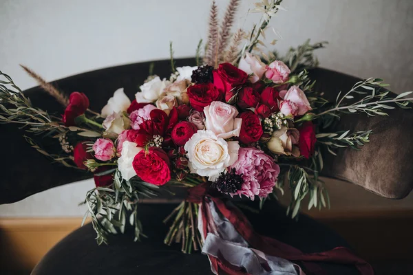 Boda. Boutonniere. Grano. Obras de arte. Un ramo de flores rojas, flores rosadas y vegetación con cintas de seda está en la silla negra —  Fotos de Stock