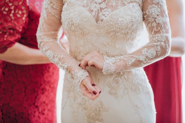 Wedding. Bouquet. Bride. Grain. Artwork. The bride in a white dress standing and straightens sleeve. Bridesmaids in red dresses are helping the bride