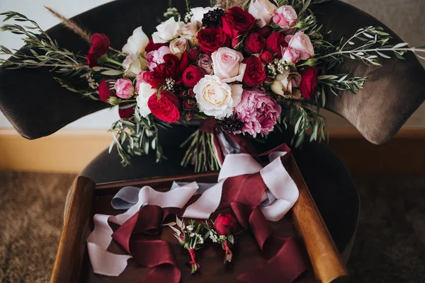 Wedding. Boutonniere. Grain. Artwork. A bouquet of red flowers, pink flowers and greenery with silk ribbons is in the black chair, boutonnieres lie next to a bouquet — Stock Photo, Image