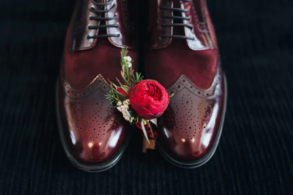 Hochzeit. Bräutigam Schuhe. boutonniere. Kunstwerk. Getreide. Bräutigam boutonniere von roten Blumen und Grün liegt auf den Lederschuhen des Bräutigams — Stockfoto