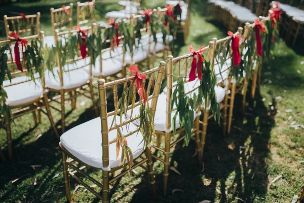 Casamento. Cerimônia. Grão. Obra. Cadeiras cor de ouro stand no gramado na área da cerimônia de casamento. Em cadeiras decoração de vegetação e fitas de tecido — Fotografia de Stock