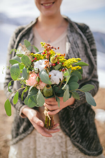 Bride holding a wedding bouquet in a rustic style on a background of snow-capped mountains