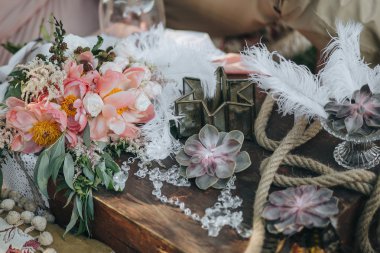 bouquet of pink and white peonies and greenery lies in an area decorated with succulents, feathers and vintage decor