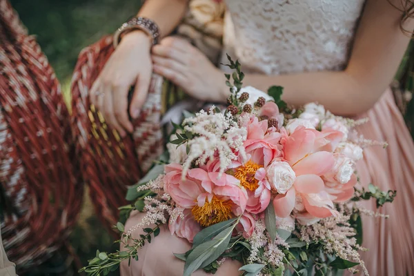 girl sitting in a wicker garden chair and holding a bouquet of pink and white peonies and green