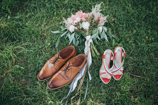 Buket peoni merah muda dan putih dan hijau tergeletak di rumput dengan sepatu bot yang terbuat dari kulit cokelat dan sepatu pengantin pria — Stok Foto