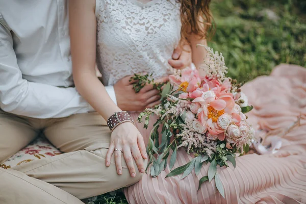 Пара сидит на траве и держит букет из розовых и белых пионов и зеленый — стоковое фото