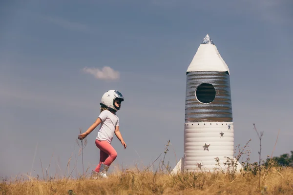 Happy child girl dressed in an astronaut costume playing with hand made rocket. Summer outdoor