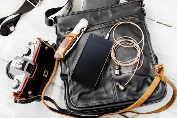 Objects on wooden background: leather bag, camera, smartphone, k