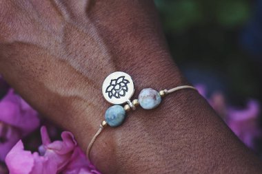 Mineral boncuk taşlı küçük bir bilezik takan bir elin açık havada çekilmiş fotoğrafı.