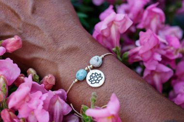 Mineral boncuk taşlı küçük bir bilezik takan bir elin açık havada çekilmiş fotoğrafı.