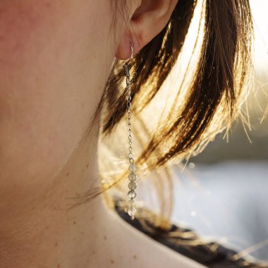 Uzun labradorit mineral taş küpe takan bir kadın kulak.