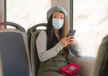 Yeni normal seyahat - genç çekici ve güzel Asyalı yüzlü Japon kadın tren vagonunda cam kenarına oturmuş, trende internet cep telefonu kullanıyor.