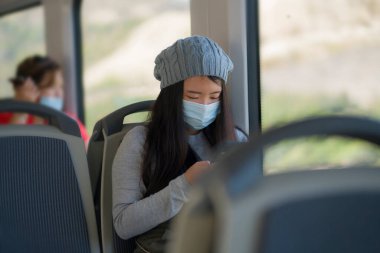 Yeni normal seyahat - çekici ve güzel Asyalı kadın yüz maskeli tren vagonunda oturuyor trende internet cep telefonu kullanıyor rahat