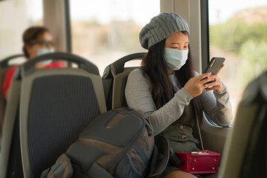 Yeni normal seyahat - çekici ve güzel Asyalı kadın yüz maskeli tren vagonunda oturuyor trende internet cep telefonu kullanıyor rahat