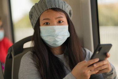 Yeni normal seyahat - çekici ve güzel Asyalı kadın yüz maskeli, tren vagonunda pencere kenarına oturmuş, trende internet cep telefonu kullanıyor.