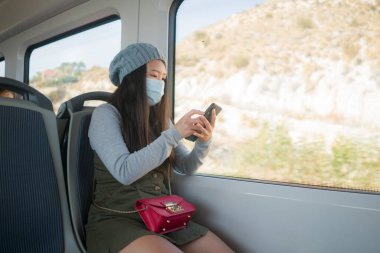 Yeni normal seyahat - genç çekici ve güzel Asyalı yüzlü Japon kadın tren vagonunda cam kenarına oturmuş, trende internet cep telefonu kullanıyor.