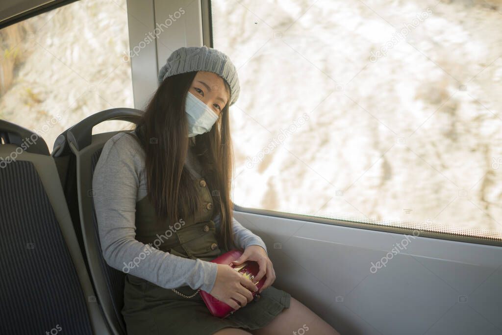 new normal traveling - young attractive and pretty Asian Korean woman in face mask sitting on railcar by window enjoying trip in the train relaxed and thoughtful