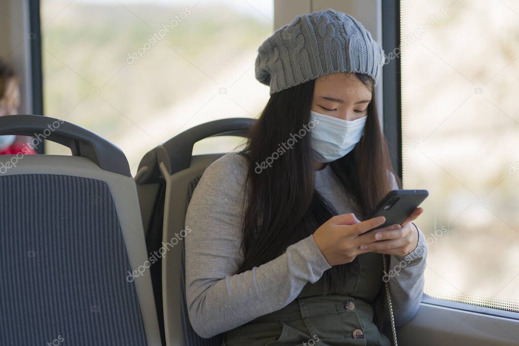 new normal traveling - young attractive and pretty Asian Chinese woman in face mask sitting on railcar by window using internet mobile phone in the train relaxed