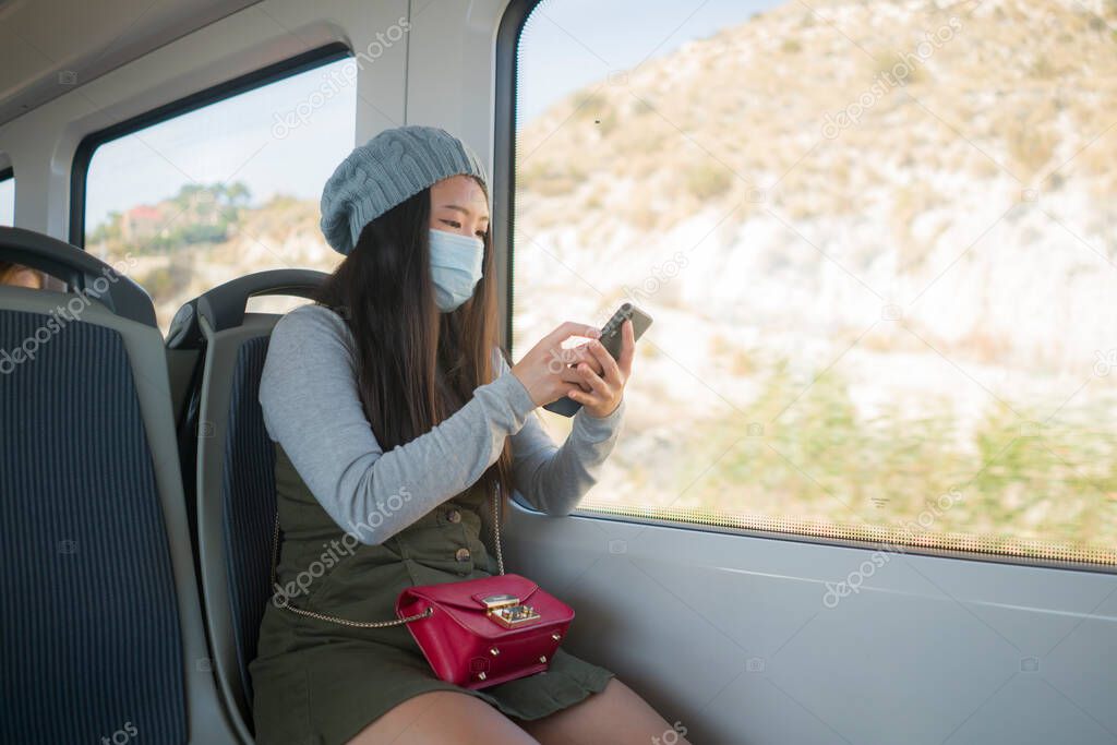 new normal traveling - young attractive and pretty Asian Japanese woman in face mask sitting on railcar by window using internet mobile phone in the train relaxed