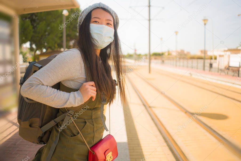 young happy and attractive Asian woman traveling during new normal - beautiful Korean girl with backpack waiting for train at station platform as tourism in virus time