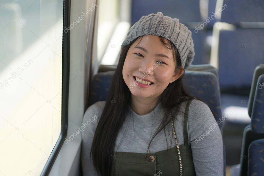 lifestyle portrait of young happy and beautiful Asian Japanese woman excited and cheerful looking through window sitting on train enjoying landscape from the railcar glass