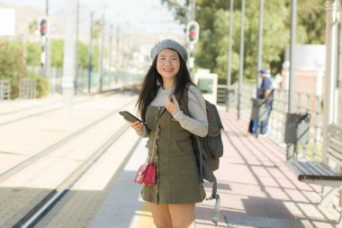 Dışarıda, tren istasyonunda sırt çantasıyla tatil ve tatil için bekleyen mutlu ve güzel Asyalı Japon turist kadının portresi.