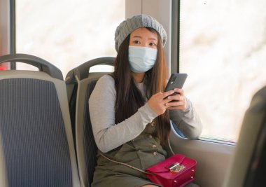 Yeni normal seyahat - genç çekici ve güzel Asyalı yüzlü Japon kadın tren vagonunda cam kenarına oturmuş, trende internet cep telefonu kullanıyor.