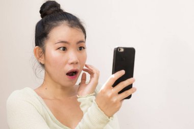 Çekici ve tatlı Asyalı Koreli kadın iletişim konseptinde izole edilmiş internet cep telefonunu kullanarak şok oldu ve şaşırdı.