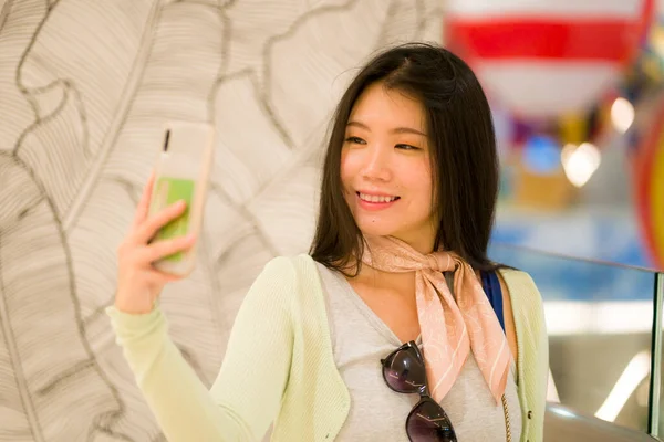 lifestyle portrait of young beautiful and happy Asian Korean woman taking selfie picture with mobile phone posing cheerful and cool in beauty and fashion concept