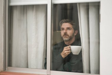 Çekici üzgün ve depresif orta yaşlı bir adamın dramatik portresi. Ev penceresinden bakan endişeli ve umutsuz acı çeken depresyon sorunu düşünceli. 