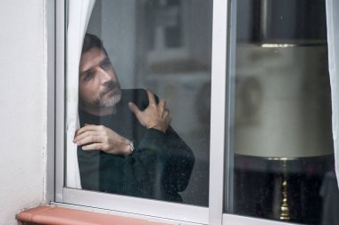 Çekici üzgün ve depresif orta yaşlı bir adamın dramatik portresi. Ev penceresinden bakan endişeli ve umutsuz acı çeken depresyon sorunu düşünceli. 