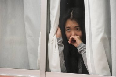 Evde stresli bir kız - üzgün ve depresif Asyalı genç bir kadının dramatik portresi. Pencerede endişeli ve çaresiz hissediyordu.