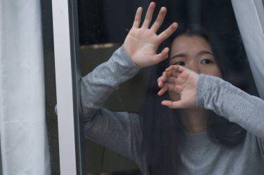 Evde stresli bir kız - üzgün ve depresif bir Asyalı kadının dramatik portresi pencerenin önünde endişeli ve umutsuz hissediyordu.
