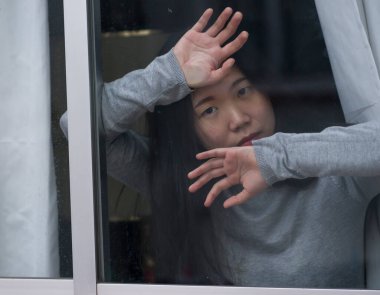 Evde stresli bir kız - üzgün ve depresif Asyalı genç bir kadının dramatik portresi. Pencerede endişeli ve çaresiz hissediyordu.