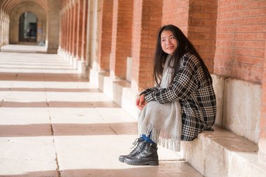 Genç ve güzel Asyalı Çinli turist kadının hayat tarzı portresi mutlu bir şekilde gülümsüyor. Güneşli bir kış günü, tatil ve turizm için tarihi bir bölgede geziniyor.