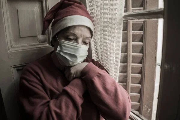 senior woman having sad Christmas alone during covid19 - mature retired lady 60s or 70s in Santa Claus hat looking depressed and emotional at home feeling lonely and melancholic