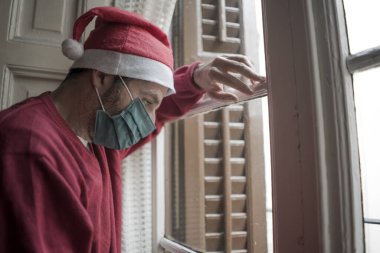 Noel Baba şapkalı ve maskeli depresif ve yorgun bir adam, yalnız başına Coronavirus yasağı yüzünden acı çekiyor.