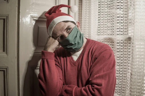 sad and lonely Christmas lockdown during covid19 - depressed and tired man in Santa Claus hat and face mask home alone suffering coronavirus restrictions missing family