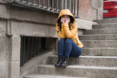 Çekici, üzgün ve depresif Koreli bir kadının dramatik yaşam tarzı portresi. Kışlık ceketli, sokak köşesindeki merdivenlerde oturmuş depresyon sorunu yaşıyor. Çaresiz hissediyor.