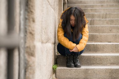 Çekici, üzgün ve depresif Koreli bir kadının dramatik yaşam tarzı portresi. Kışlık ceketli, sokak köşesindeki merdivenlerde oturmuş depresyon sorunu yaşıyor. Çaresiz hissediyor.