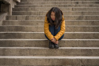 Çekici, üzgün ve depresif Koreli bir kadının dramatik yaşam tarzı portresi. Kışlık ceketli, sokak köşesindeki merdivenlerde oturmuş depresyon sorunu yaşıyor. Çaresiz hissediyor.