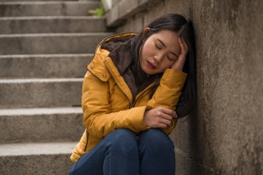 Çekici, üzgün ve depresif Koreli bir kadının dramatik yaşam tarzı portresi. Kışlık ceketli, sokak köşesindeki merdivenlerde oturmuş depresyon sorunu yaşıyor. Çaresiz hissediyor.