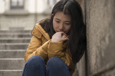 Çekici, üzgün ve depresif Koreli bir kadının dramatik yaşam tarzı portresi. Kışlık ceketli, sokak köşesindeki merdivenlerde oturmuş depresyon sorunu yaşıyor. Çaresiz hissediyor.